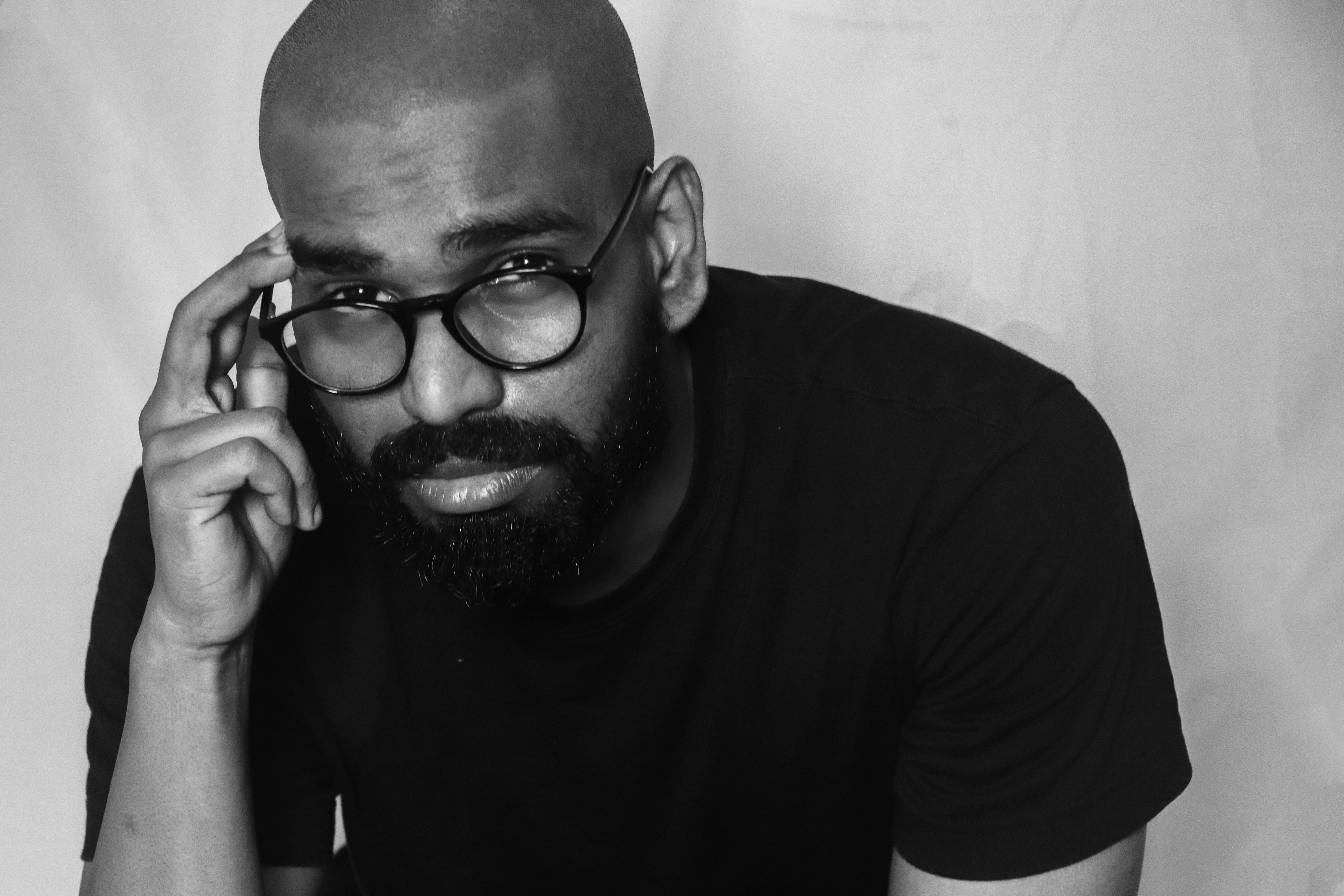 Black and white portrait of a bearded, bald man wearing eyeglasses with a serious expression.